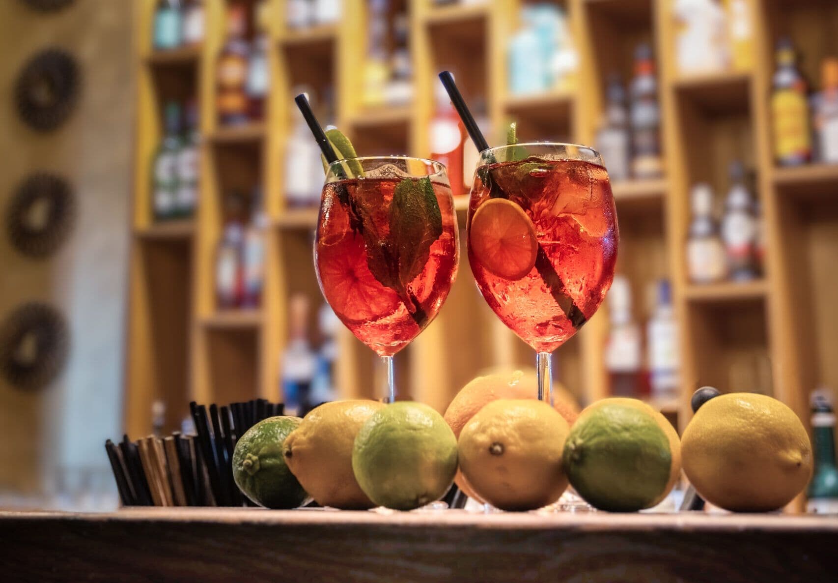Kaks spritz'i baarileti peal, ees tsitrused, taga pudeliriiulid